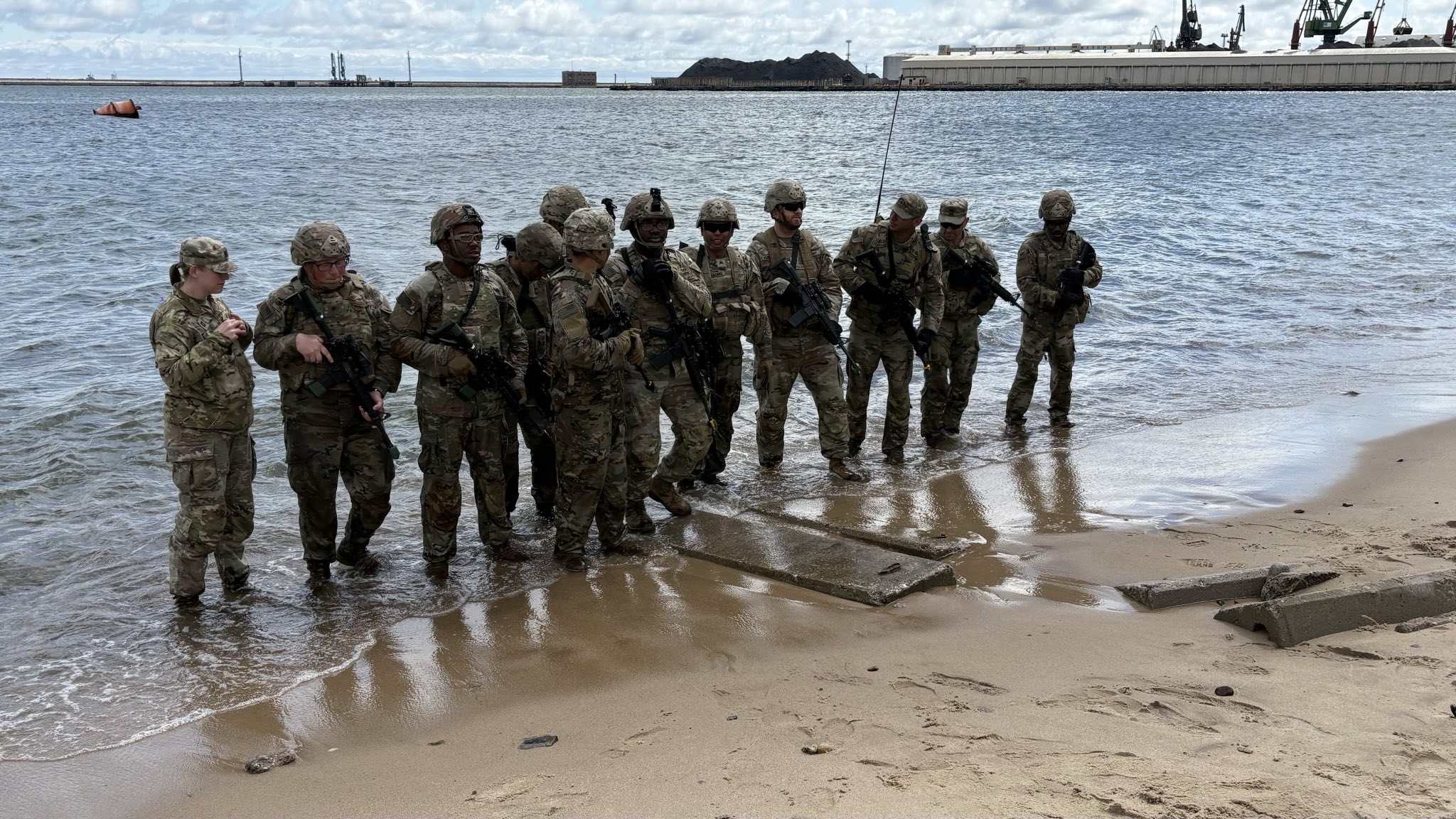 Twelve uniformed men and women from the US Army and Polish Armed Forces standing at the edge of the beach in the water.