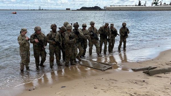 Twelve uniformed men and women from the US Army and Polish Armed Forces standing at the edge of the beach in the water.