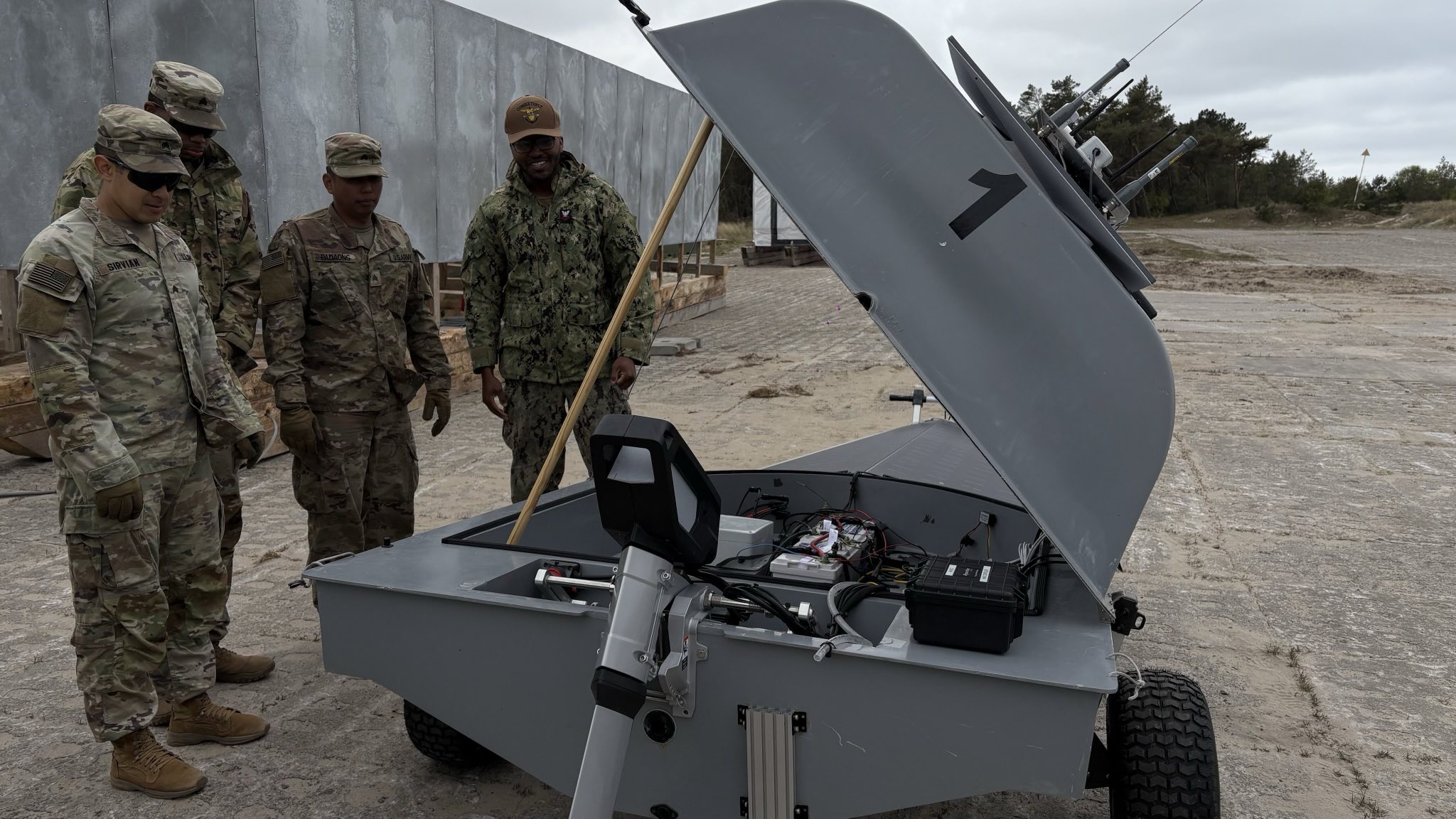 Four uniformed men from the US Army and Polish Armed Forces viewing the inside of a proped up Unmanned Naval Innoation Team (UNIT).