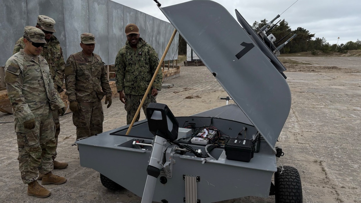 Four uniformed men from the US Army and Polish Armed Forces viewing the inside of a proped up Unmanned Naval Innoation Team (UNIT).
