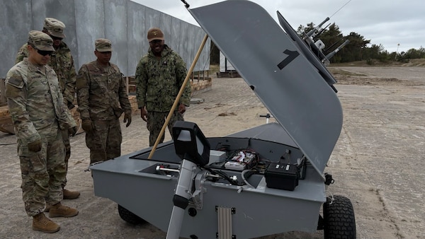 Four uniformed men from the US Army and Polish Armed Forces viewing the inside of a proped up Unmanned Naval Innoation Team (UNIT).