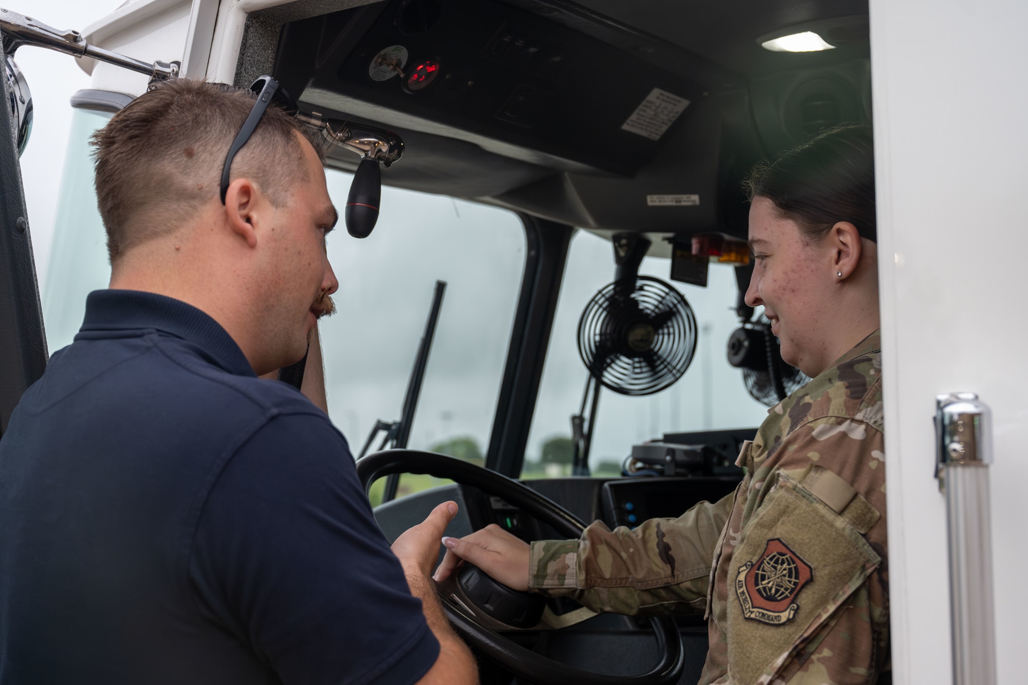 Fire Lt. Robert Griffin, 22nd Civil Engineer Squadron driver operator, provides a firetruck cabin tour for Airman 1st Class Haley Margavich, 22nd Air Refueling Wing religious affairs Airman, during a chapel visit to the base fire station at McConnell Air Force Base, Kansas, July 18, 2025. Unit engagement builds relationships and a better understanding of a variety of missions. (U.S. Air Force photo by Airman 1st Class Paula Arce)