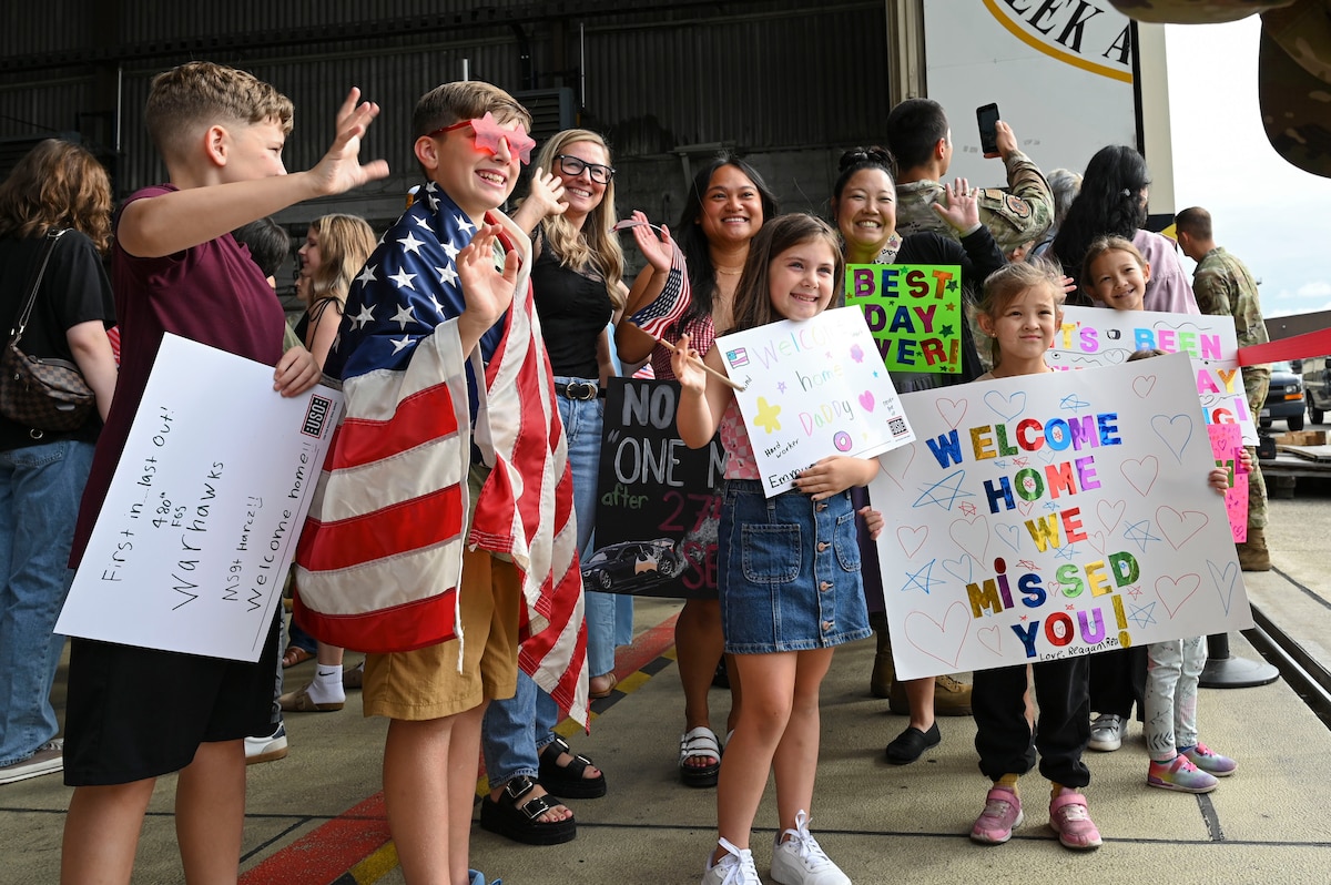 Children hold an American flag and welcome home signs