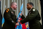 Two men wearing military uniforms hold a blue flag on a flagpole.