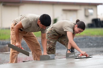 U.S. Air Force Airman 1st Class Lynn El Helou, a structural specialist with the 102nd Civil Engineer Squadron (CES), right, and U.S. Air Force Airman 1st Class Eric Davila, a member of the Rapid Engineer Deployable, Heavy Operational Repair Squadron, Engineer (RED HORSE) Squadron, smooth concrete during a deployment for training (DFT) on Yokota Air Base, Japan, July 3, 2025.