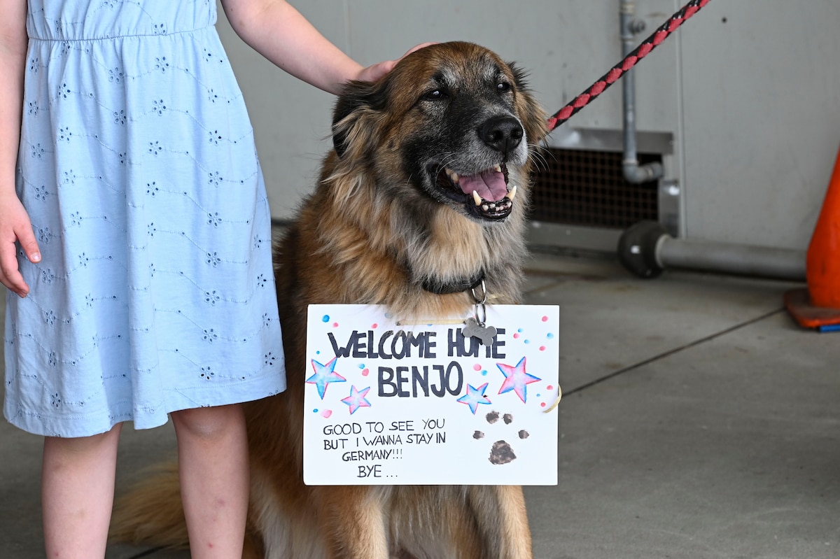 A dog with a welcome home sign on its collar sits by its owner.