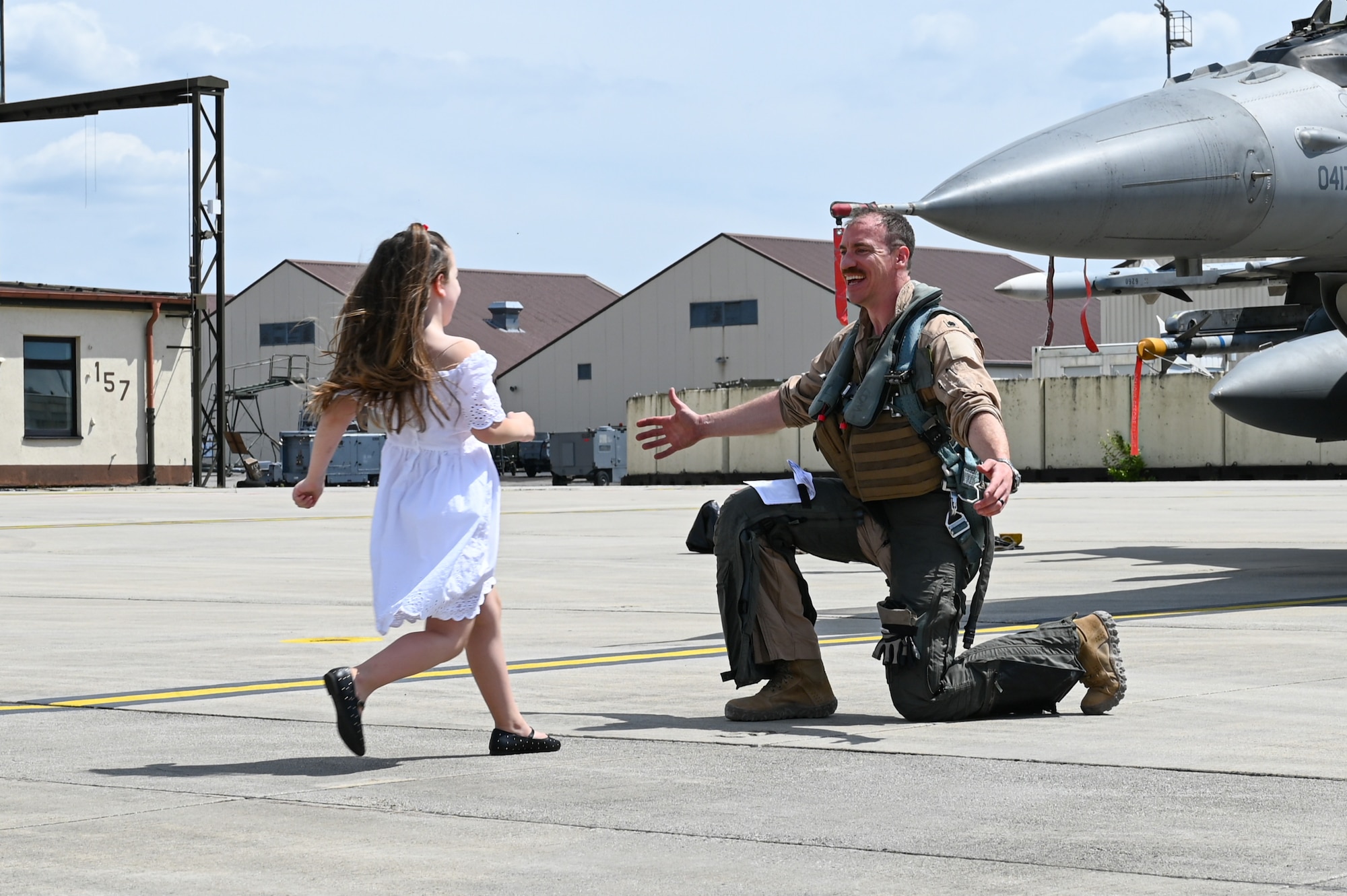 A child runs to a fighter pilot kneeling on the ground with open arms.