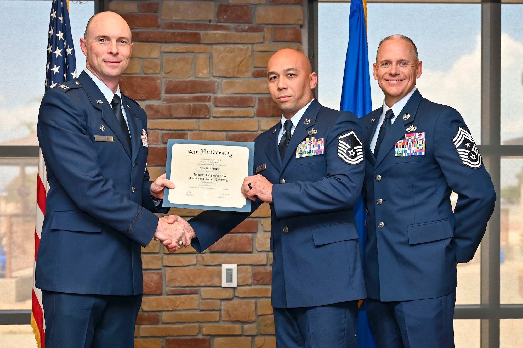 U.S. Air Force Master Sgt. Gene San Nicholas of the 849th Aircraft Maintenance Squadron, Community College of the Air Force Graduate, center, accepts an Associate of Applied Science Degree from U.S. Air Force Col. John Ethridge, 49th Wing commander, left, and U.S. Air Force Chief Master Sgt. William Ford, 49th Wing command chief, during a CCAF graduation at Holloman Air Force Base, New Mexico, July 11, 2025. Each enlisted Airman has the opportunity to earn a career-focused associate degree through the CCAF, empowering them to grow professionally while supporting the mission. (U.S. Air Force photo by Senior Airman Michelle Ferrari)
