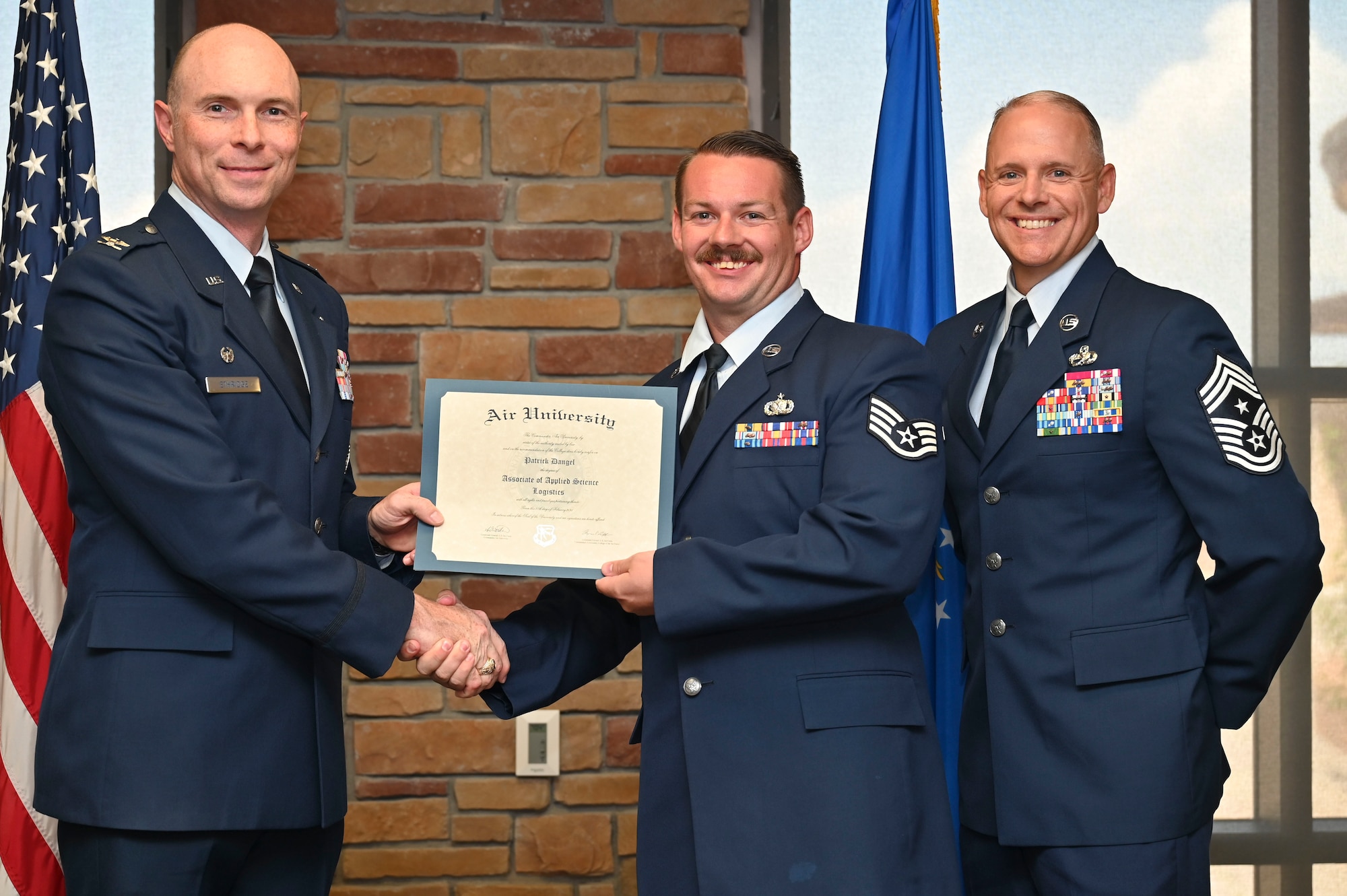 U.S. Air Force Staff Sgt. Patrick Dangel of the 635th Materiel Maintenance Support Squadron, Community College of the Air Force Graduate, center, accepts an Associate of Applied Science Degree from U.S. Air Force Col. John Ethridge, 49th Wing commander, left, and U.S. Air Force Chief Master Sgt. William Ford, 49th Wing command chief, during the graduation of CCAF at Holloman Air Force Base, New Mexico, July 11, 2025. Each enlisted Airman has the opportunity to earn a career-focused associate degree through the CCAF, empowering them to grow professionally while supporting the mission. (U.S. Air Force photo by Senior Airman Michelle Ferrari)