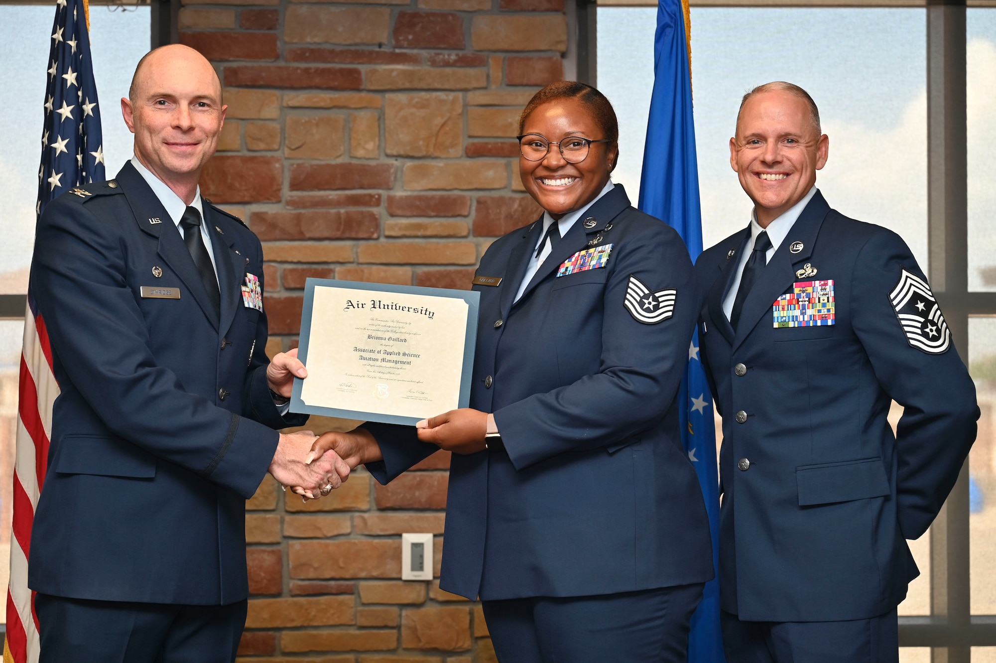 U.S. Air Force Tech. Sgt. Brionna Gaillard of the 49th Mission Support Group, Community College of the Air Force Graduate, center, accepts an Associate of Applied Science Degree from U.S. Air Force Col. John Ethridge, 49th Wing commander, left, and U.S. Air Force Chief Master Sgt. William Ford, 49th Wing command chief, during the graduation of CCAF at Holloman Air Force Base, New Mexico, July 11, 2025. Each enlisted Airman has the opportunity to earn a career-focused associate degree through the CCAF, the only degree-granting institution in the Department of Defense, empowering them to grow professionally while supporting the mission. (U.S. Air Force photo by Senior Airman Michelle Ferrari)