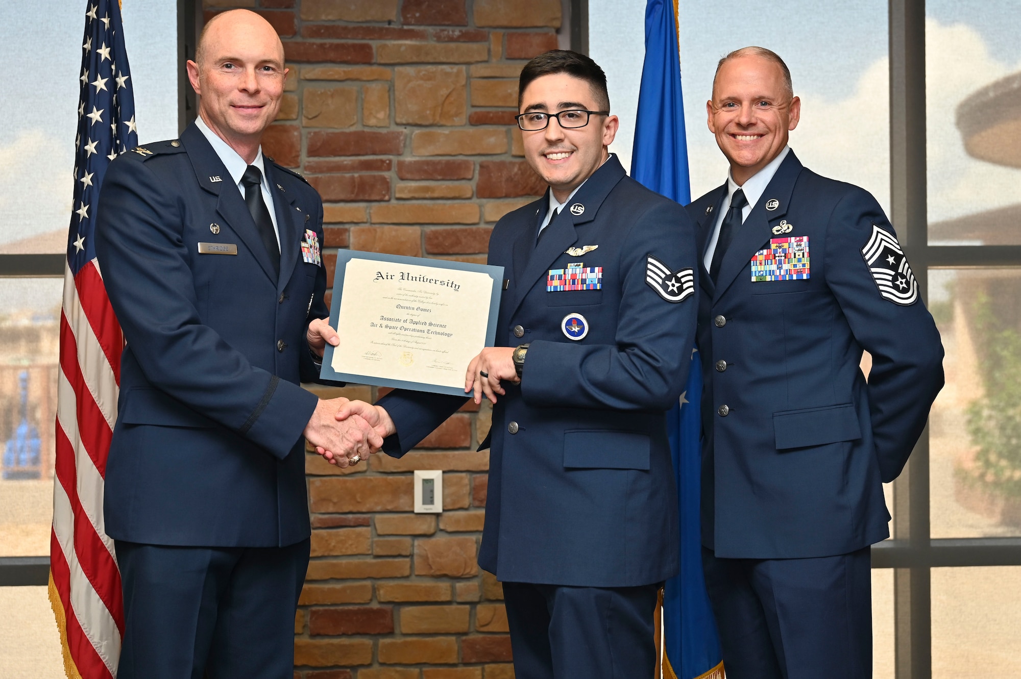 U.S. Air Force Tech. Sgt. Quentin Gomez of the 6th Attack Squadron, Community College of the Air Force Graduate, center, accepts an Associate of Applied Science Degree from U.S. Air Force Col. John Ethridge, 49th Wing commander, left, and U.S. Air Force Chief Master Sgt. William Ford, 49th Wing command chief, during the graduation of CCAF at Holloman Air Force Base, New Mexico, July 11, 2025. Each enlisted Airman has the opportunity to earn a career-focused associate degree through the CCAF, empowering them to grow professionally while supporting the mission. (U.S. Air Force photo by Senior Airman Michelle Ferrari)