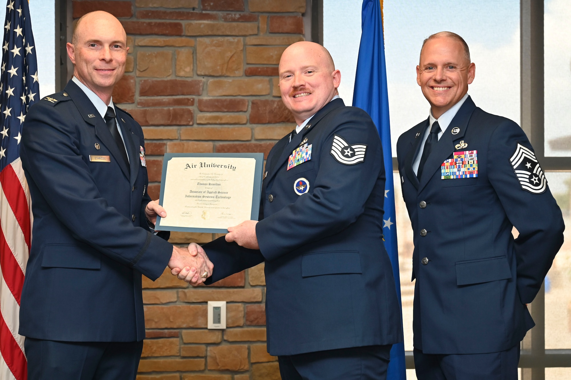 U.S. Air Force Tech. Sgt. Thomas Hamilton of the 49th Logistics Readiness Squadron, Community College of the Air Force Graduate, center, accepts an Associate of Applied Science Degree from U.S. Air Force Col. John Ethridge, 49th Wing commander, left, and U.S. Air Force Chief Master Sgt. William Ford, 49th Wing command chief, during the graduation of CCAF at Holloman Air Force Base, New Mexico, July 11, 2025. Each enlisted Airman has the opportunity to earn a career-focused associate degree through the CCAF, the only degree-granting institution in the Department of Defense, empowering them to grow professionally while supporting the mission. (U.S. Air Force photo by Senior Airman Michelle Ferrari)