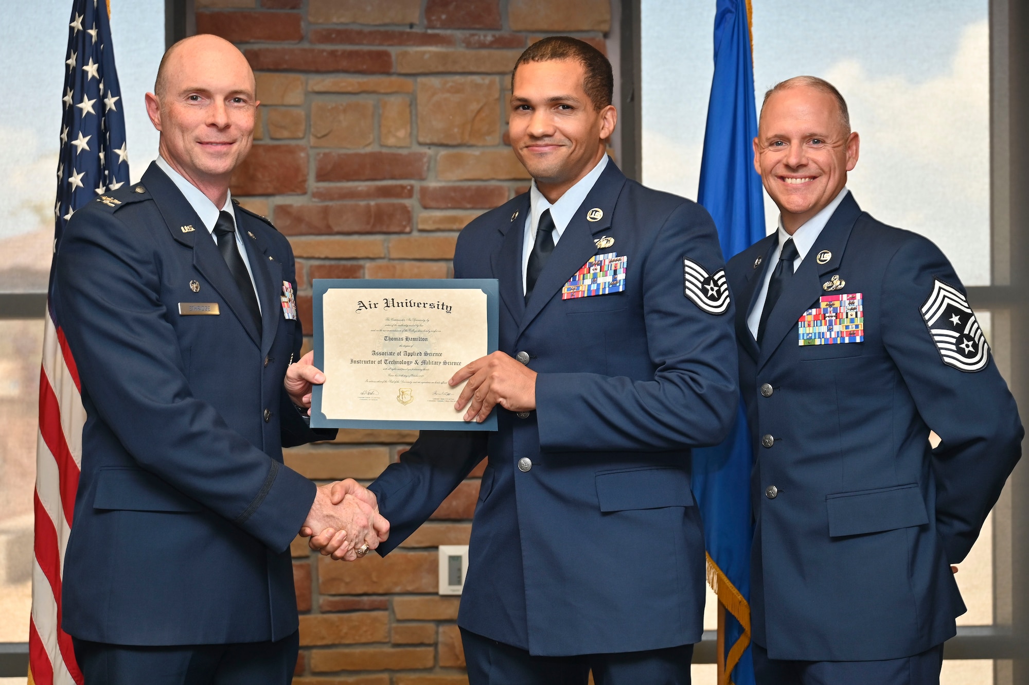 U.S. Air Force Tech. Sgt. Brandon Harper of the 49th Communications Squadron, Community College of the Air Force Graduate, center, accepts Associate of an Applied Science Degree from U.S. Air Force Col. John Ethridge, 49th Wing commander, left, and U.S. Air Force Chief Master Sgt. William Ford, 49th Wing command chief, during the graduation of CCAF at Holloman Air Force Base, New Mexico, July 11, 2025. Each enlisted Airman has the opportunity to earn a career-focused associate degree through the CCAF, the only degree-granting institution in the Department of Defense, empowering them to grow professionally while supporting the mission. (U.S. Air Force photo by Senior Airman Michelle Ferrari)
