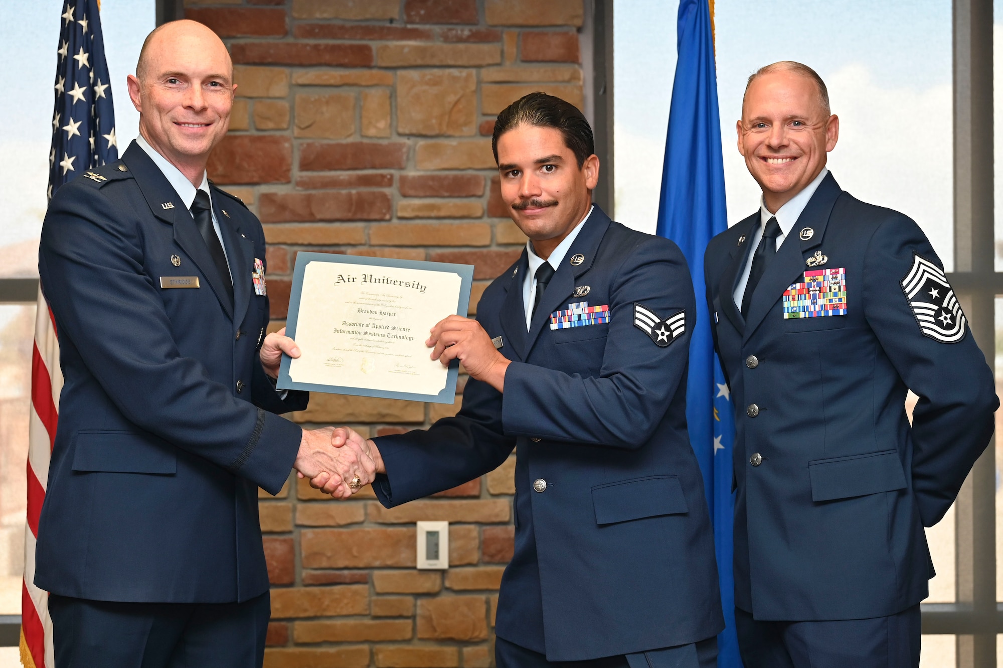 U.S. Air Force Tech. Senior Airman Christopher Hilraldo-Rivera of the 635th Materiel Maintenance Squadron, Community College of the Air Force Graduate, center, accepts an Associate of Applied Science Degree from U.S. Air Force Col. John Ethridge, 49th Wing commander, left, and U.S. Air Force Chief Master Sgt. William Ford, 49th Wing command chief, during the graduation of CCAF at Holloman Air Force Base, New Mexico, July 11, 2025. Each enlisted Airman has the opportunity to earn a career-focused associate degree through the CCAF, empowering them to grow professionally while supporting the mission. (U.S. Air Force photo by Senior Airman Michelle Ferrari)