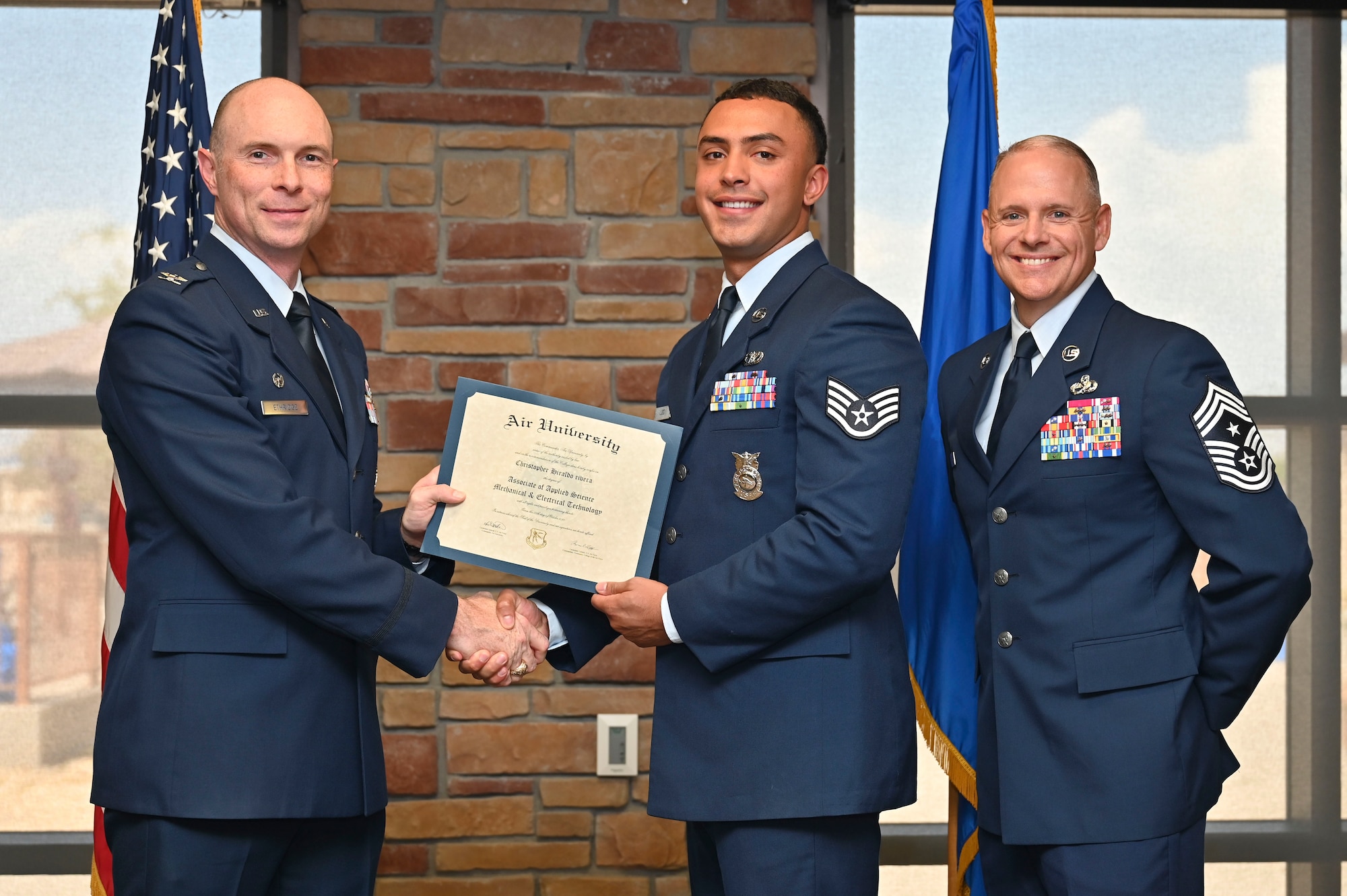 U.S. Air Force Staff. Sgt. Izaien Lugo of the 49th Civil Engineer Squadron, Community College of the Air Force Graduate, center, accepts an Associate of Applied Science Degree from U.S. Air Force Col. John Ethridge, 49th Wing commander, left, and U.S. Air Force Chief Master Sgt. William Ford, 49th Wing command chief, during the graduation of CCAF at Holloman Air Force Base, New Mexico, July 11, 2025. Each enlisted Airman has the opportunity to earn a career-focused associate degree through the CCAF, the only degree-granting institution in the Department of Defense, empowering them to grow professionally while supporting the mission. (U.S. Air Force photo by Senior Airman Michelle Ferrari)