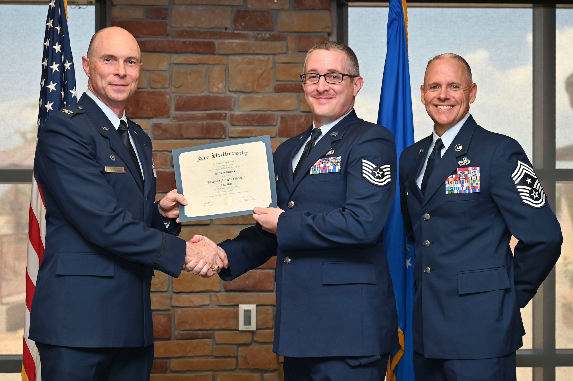 U.S. Air Force Tech. Sgt. William McCrea of the 49th Logistics Readiness Squadron, Community College of the Air Force Graduate, center, accepts an Associate of Applied Science Degree from U.S. Air Force Col. John Ethridge, 49th Wing commander, left, and U.S. Air Force Chief Master Sgt. William Ford, 49th Wing command chief, during the graduation of CCAF at Holloman Air Force Base, New Mexico, July 11, 2025. Each enlisted Airman has the opportunity to earn a career-focused associate degree through the CCAF, empowering them to grow professionally while supporting the mission. (U.S. Air Force photo by Senior Airman Michelle Ferrari)