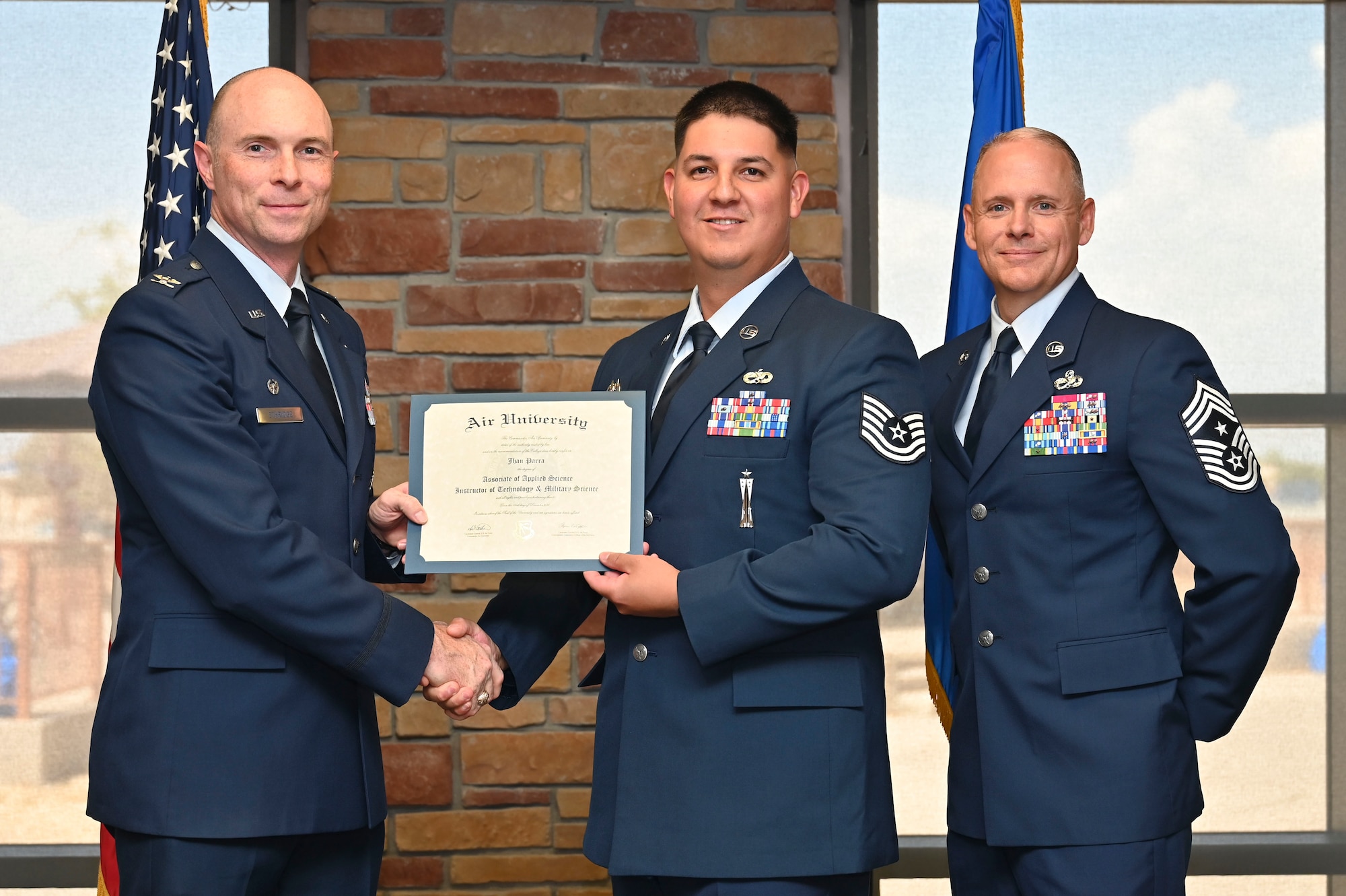U.S. Air Force Tech. Sgt. Jhan Parra of the 49th Wing, Community College of the Air Force Graduate, center, accepts an Associate of Applied Science Degree from U.S. Air Force Col. John Ethridge, 49th Wing commander, left, and U.S. Air Force Chief Master Sgt. William Ford, 49th Wing command chief, during the graduation of CCAF at Holloman Air Force Base, New Mexico, July 11, 2025. Each enlisted Airman has the opportunity to earn a career-focused associate degree through the CCAF, the only degree-granting institution in the Department of Defense, empowering them to grow professionally while supporting the mission. (U.S. Air Force photo by Senior Airman Michelle Ferrari)