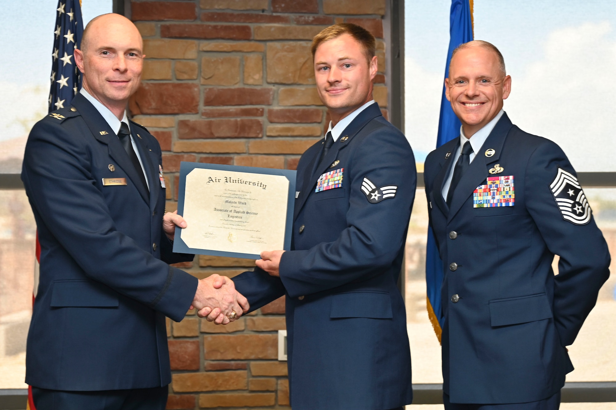 U.S. Air Force Senior Airman Malachi Ward of 49th Logistics Readiness Squadron, Community College of the Air Force Graduate, center, accepts an Associate of Applied Science Degree from U.S. Air Force Col. John Ethridge, 49th Wing commander, left, and U.S. Air Force Chief Master Sgt. William Ford, 49th Wing command chief, during the graduation of CCAF at Holloman Air Force Base, New Mexico, July 11, 2025. Each enlisted Airman has the opportunity to earn a career-focused associate degree through the CCAF, empowering them to grow professionally while supporting the mission. (U.S. Air Force photo by Senior Airman Michelle Ferrari)