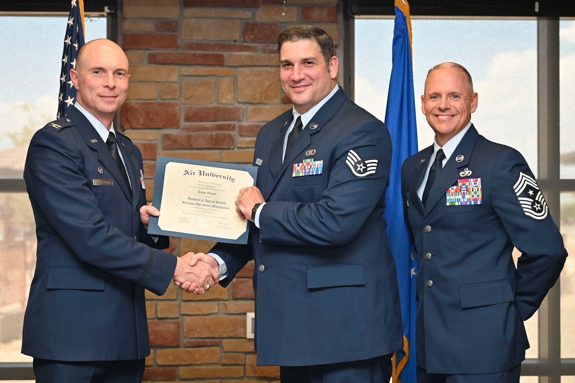 U.S. Air Force Staff Sgt. Aaron Wiener of the 7th Air Support Operations Squadron, Community College of the Air Force Graduate, center, accepts an Associate of Applied Science Degree from U.S. Air Force Col. John Ethridge, 49th Wing commander, left, and U.S. Air Force Chief Master Sgt. William Ford, 49th Wing command chief, during the graduation of CCAF at Holloman Air Force Base, New Mexico, July 11, 2025. Each enlisted Airman has the opportunity to earn a career-focused associate degree through the CCAF, the only degree-granting institution in the Department of Defense, empowering them to grow professionally while supporting the mission. (U.S. Air Force photo by Senior Airman Michelle Ferrari)