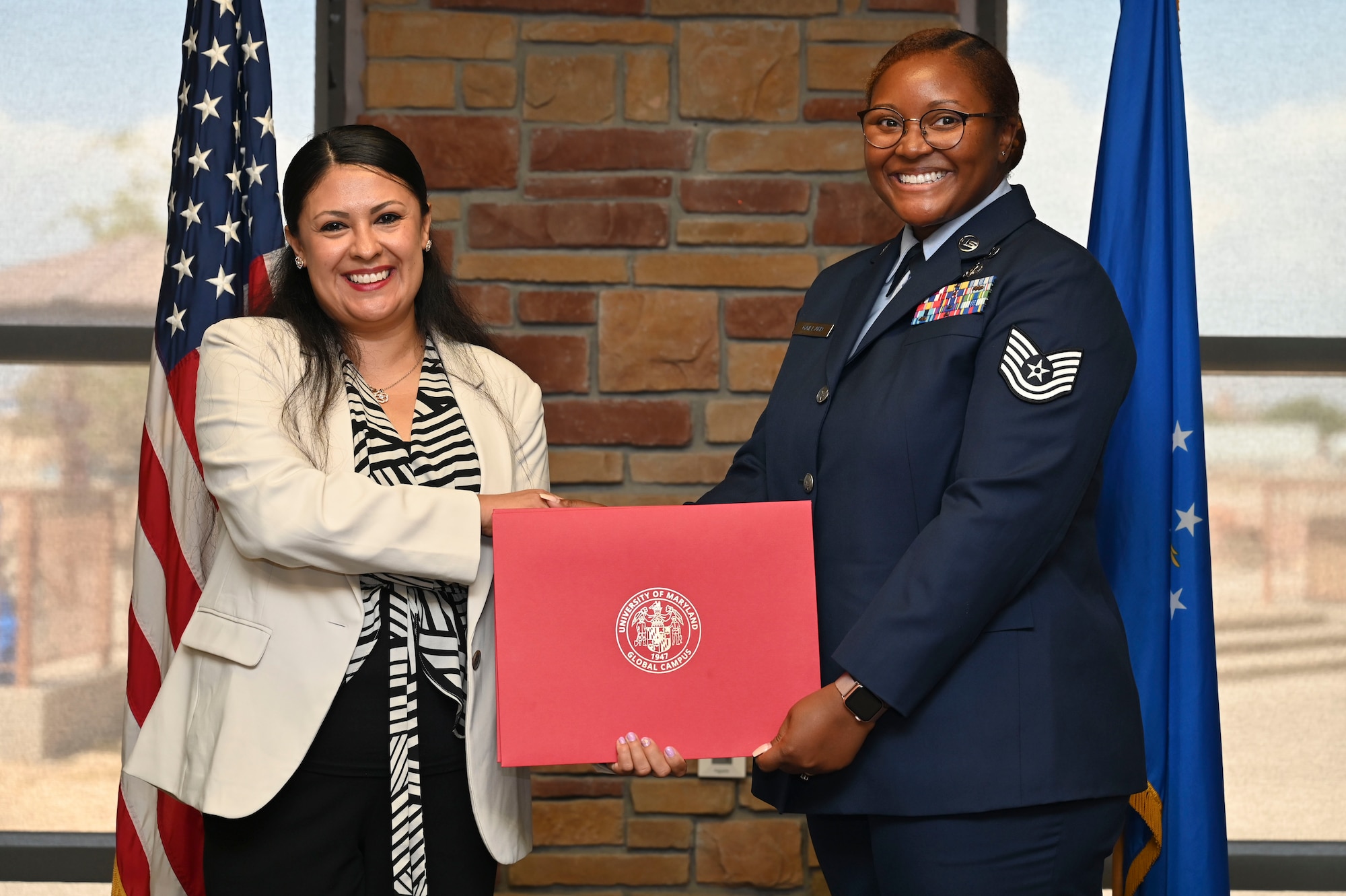 U.S. Air Force Tech. Sgt. Brionna Gaillard of the 49th Mission Support Group, University of Maryland Global Campus Graduate, right, accepts an Associate of Applied Science Degree from Kathleen Velasco, UMGC Conferral, during the graduation ceremony at Holloman Air Force Base, New Mexico, July 11, 2025. Each enlisted Airman has the opportunity to advance their education through the UMGC, which offers flexible degree programs designed to accommodate military life and support professional growth alongside the mission. (U.S. Air Force photo by Senior Airman Michelle Ferrari)