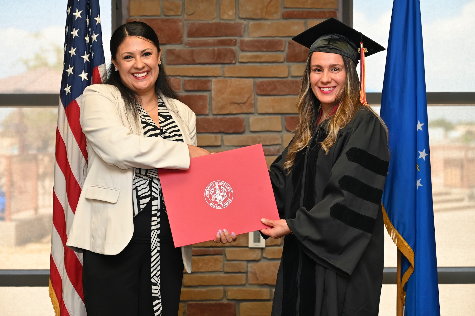 Maria Spahr of the 49th Force Support Squadron, University of Maryland Global Campus Graduate, right, accepts an Associate of Applied Science Degree from Kathleen Velasco, UMGC Conferral, during the graduation ceremony at Holloman Air Force Base, New Mexico, July 11, 2025. Each enlisted Airman has the opportunity to advance their education through the University of UMGS, which offers flexible degree programs designed to accommodate military life and support professional growth alongside the mission. (U.S. Air Force photo by Senior Airman Michelle Ferrari)