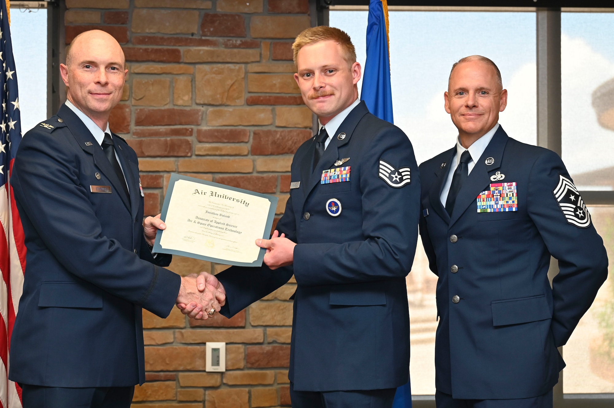 U.S. Air Force Staff Sgt. Jonathan Boland of the 16th Training Squadron, Community College of the Air Force Graduate, accepts an Associate of Applied Science Degree from U.S. Air Force Col. John Ethridge, 49th Wing commander, left, and U.S. Air Force Chief Master Sgt. William Ford, 49th Wing command chief, during the graduation of CCAF at Holloman Air Force Base, New Mexico, July 11, 2025. Each enlisted Airman has the opportunity to earn a career-focused associate degree through the CCAF, the only degree-granting institution in the Department of Defense, empowering them to grow professionally while supporting the mission. (U.S. Air Force photo by Senior Airman Michelle Ferrari)