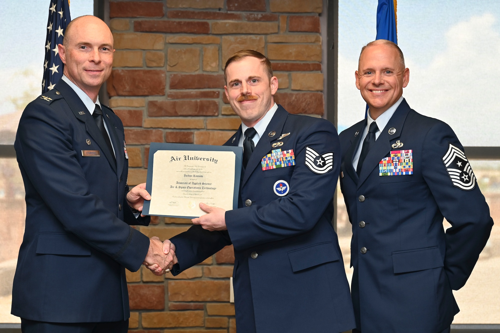 U.S. Air Force Tech. Sgt. Jordan Rossow of the 29th Attack Squadron, Community College of the Air Force Graduate, center, accepts an Associate of Applied Science Degree from U.S. Air Force Col. John Ethridge, 49th Wing commander, left, and U.S. Air Force Chief Master Sgt. William Ford, 49th Wing command chief, during the graduation of CCAF at Holloman Air Force Base, New Mexico, July 11, 2025. Each enlisted Airman has the opportunity to earn a career-focused associate degree through the CCAF, empowering them to grow professionally while supporting the mission. (U.S. Air Force photo by Senior Airman Michelle Ferrari)
