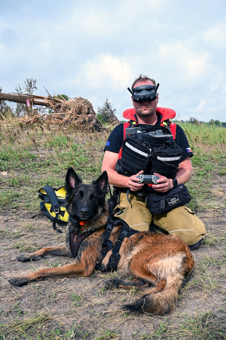 Jiri Studnicka, a drone operator with a Czech Republic emergency response team, or CZERT, kneels beside search-and-rescue dog Origami while operating a small drone along the Guadalupe River near Kerrville, Texas, July 15, 2025.