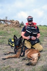 Jiri Studnicka, a drone operator with a Czech Republic emergency response team, or CZERT, kneels beside search-and-rescue dog Origami while operating a small drone along the Guadalupe River near Kerrville, Texas, July 15, 2025.