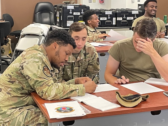 Three Airmen look down at a sheet of paper during training