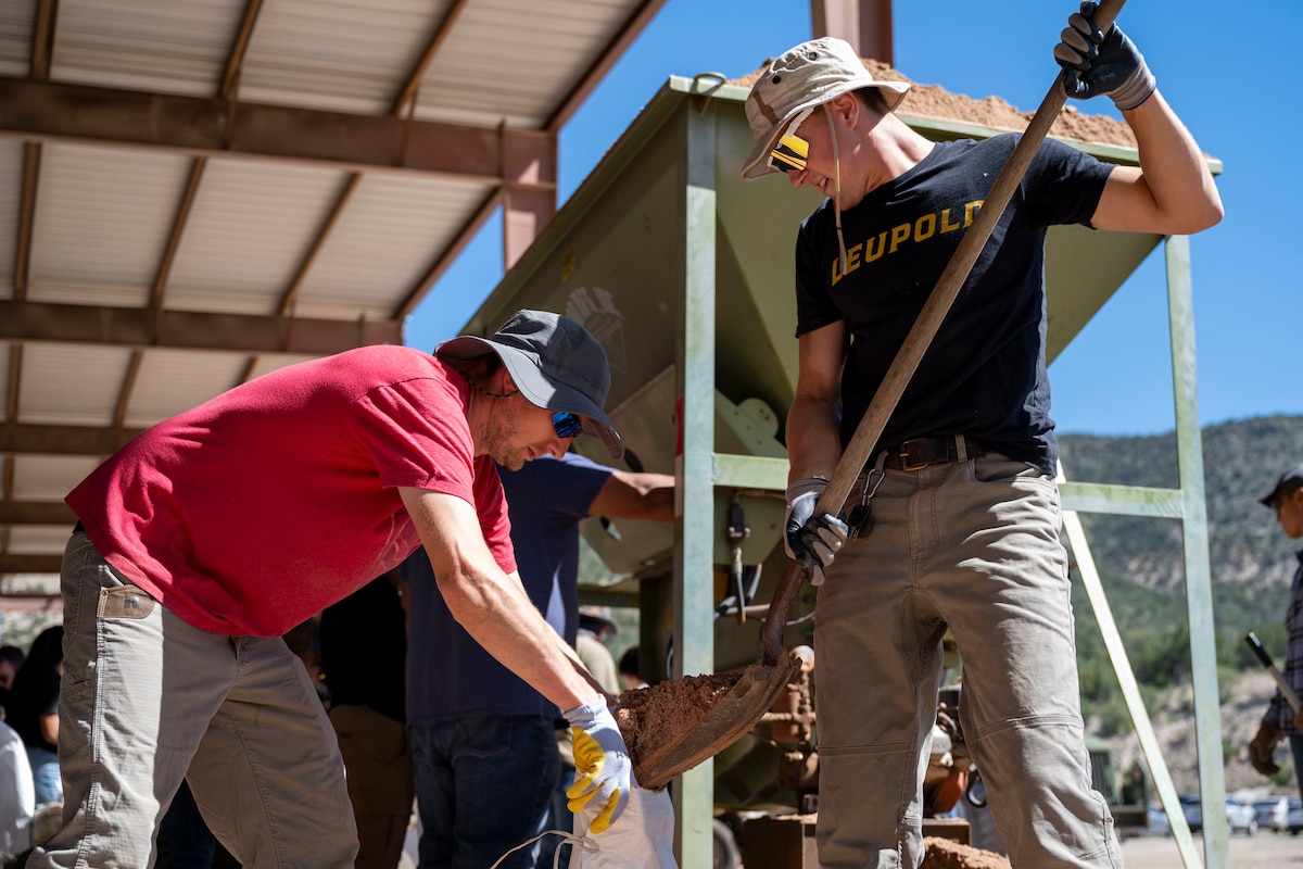 Ryan Kidrowski, Southwester Electric electrician, left, and U.S. Air Force Aidan Rodriguez, 49th Aircraft Maintenance Squadron avionics technician, fill up a sandbag at Mescalero, New Mexico, July 19, 2025.