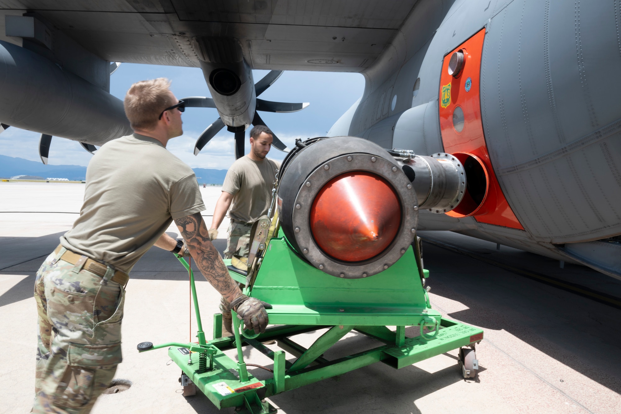 Two service members positioning a piece of equipment near a military aircraft.