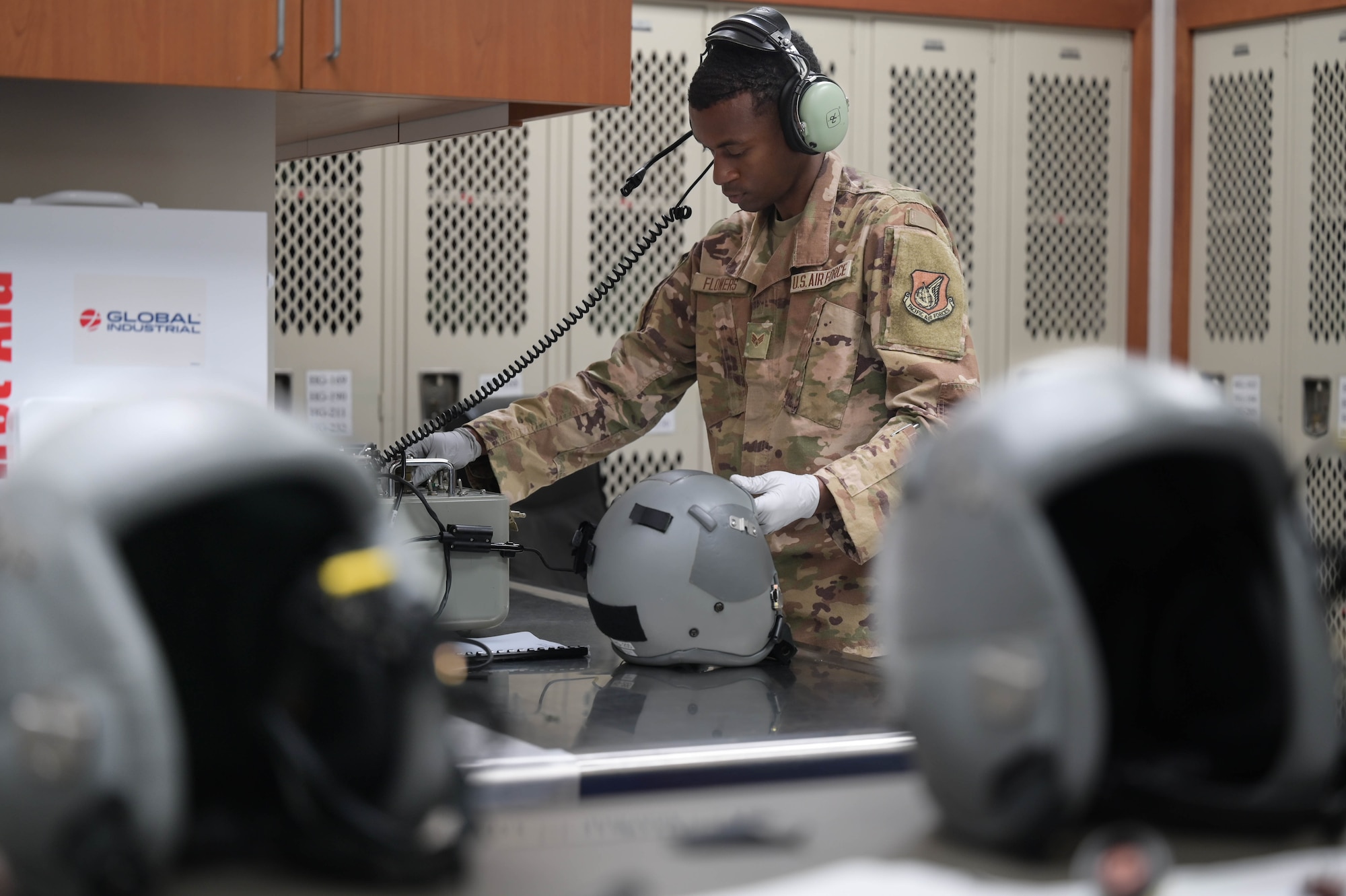 An Airman inspects the transmission on a pilot's helmet while wearing headphones.