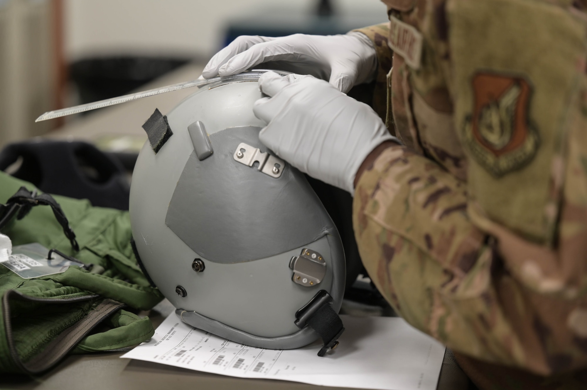 Airman with gloved hands uses a ruler to measure items on a pilot's helmet.