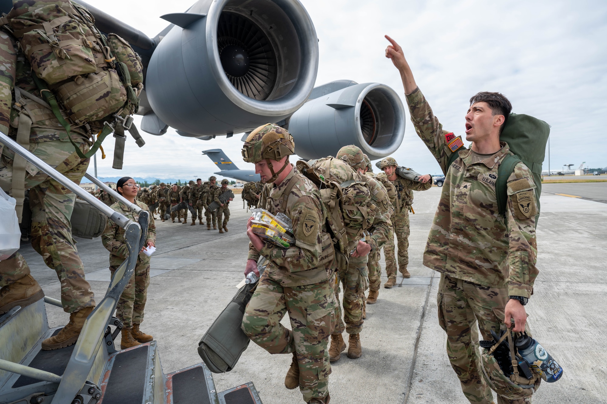 A soldier instructs personnel to enter a C-17 through a side door.