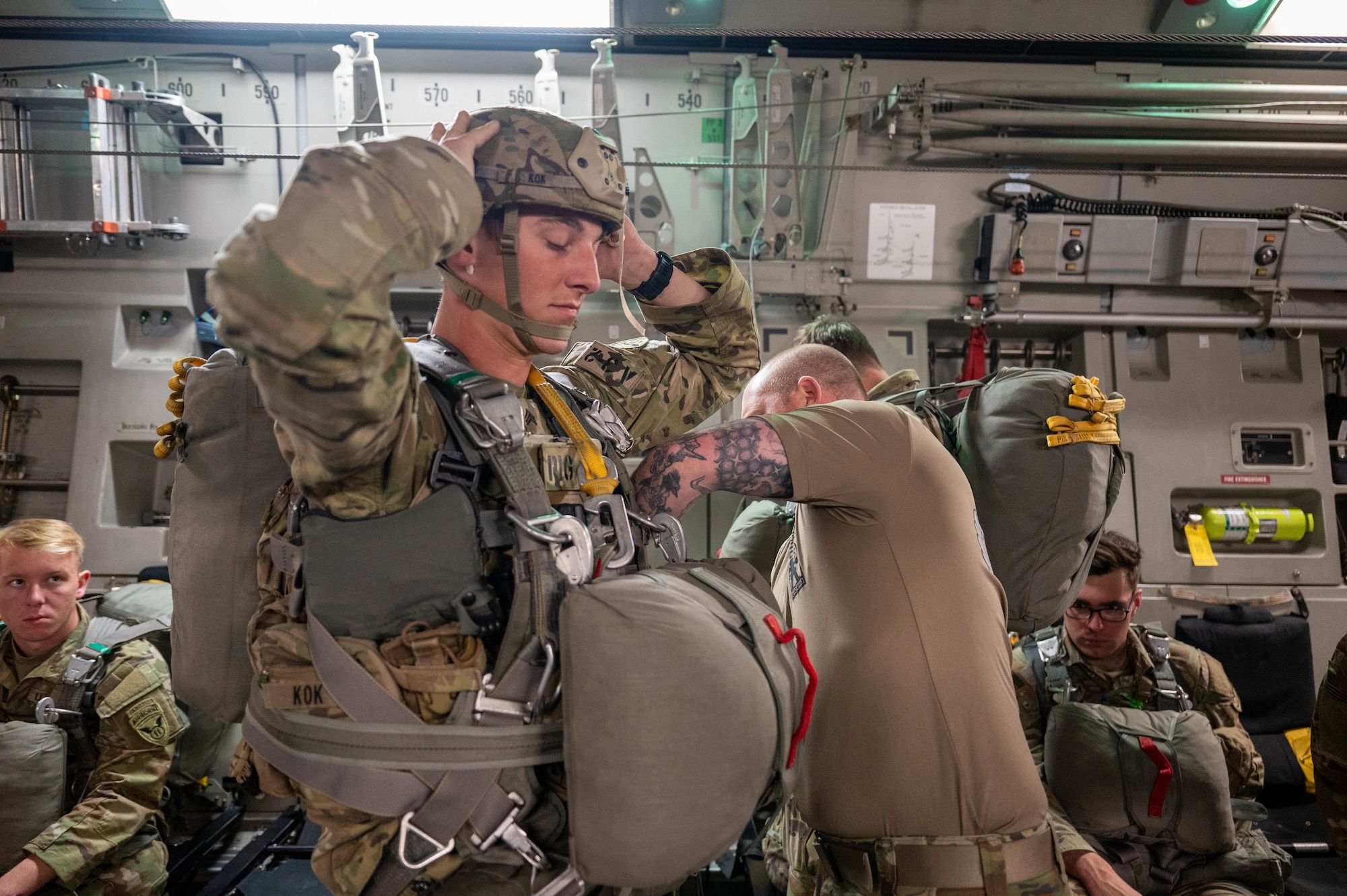 Paratrooper stands inside of a C-17, getting his jump equipment inspected by another soldier.