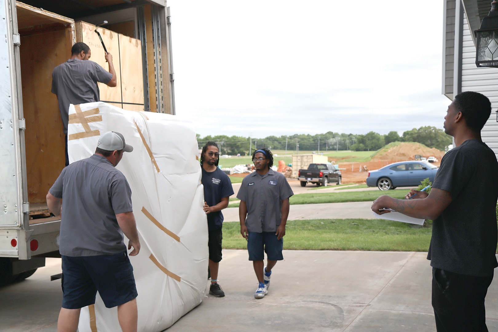 A man with a clipboard in his hand watches as several men upload a moving truck.