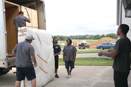 A man with a clipboard in his hand watches as several men upload a moving truck.