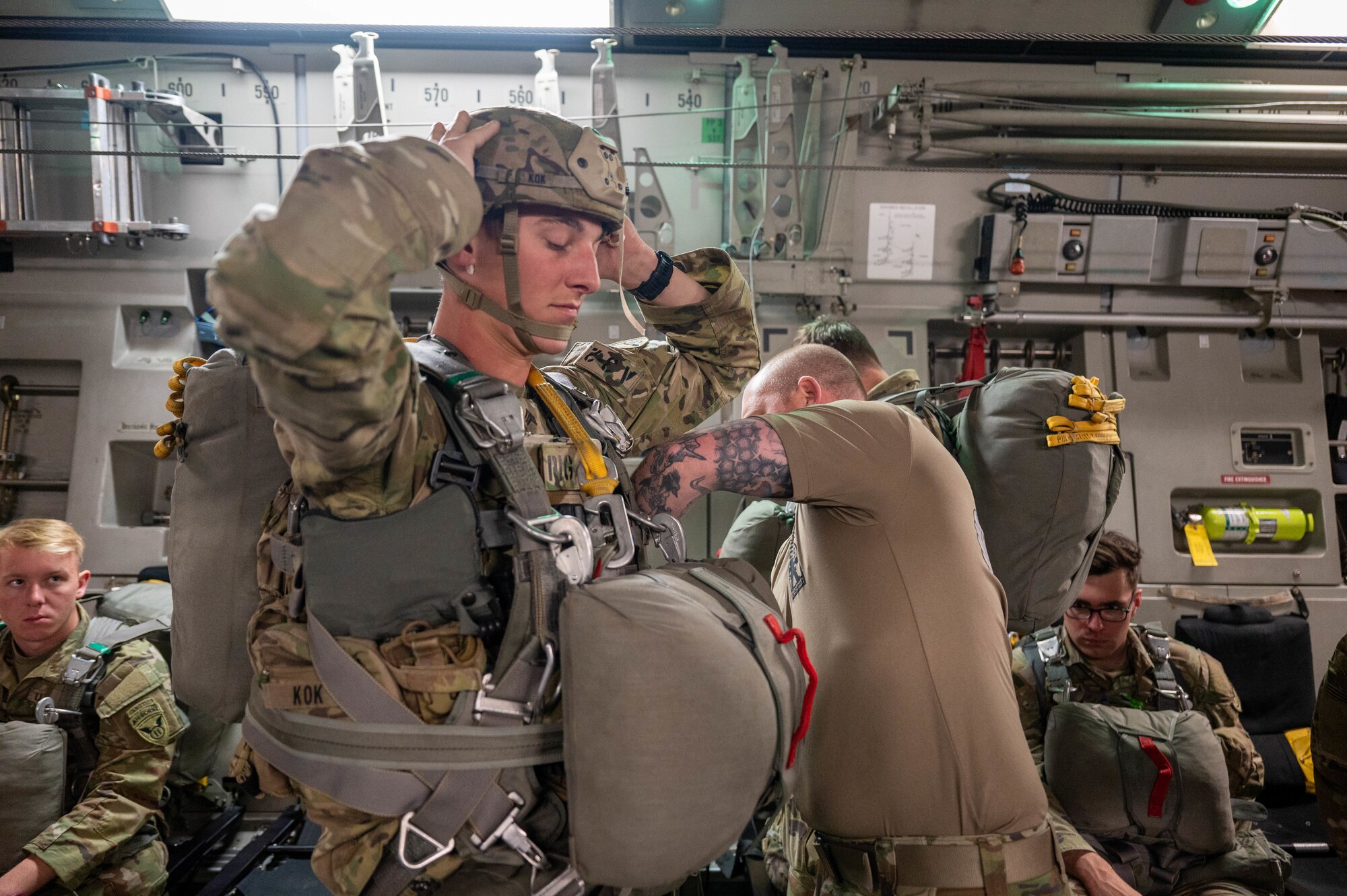 Paratrooper stands inside of a C-17, getting his jump equipment inspected by another soldier.