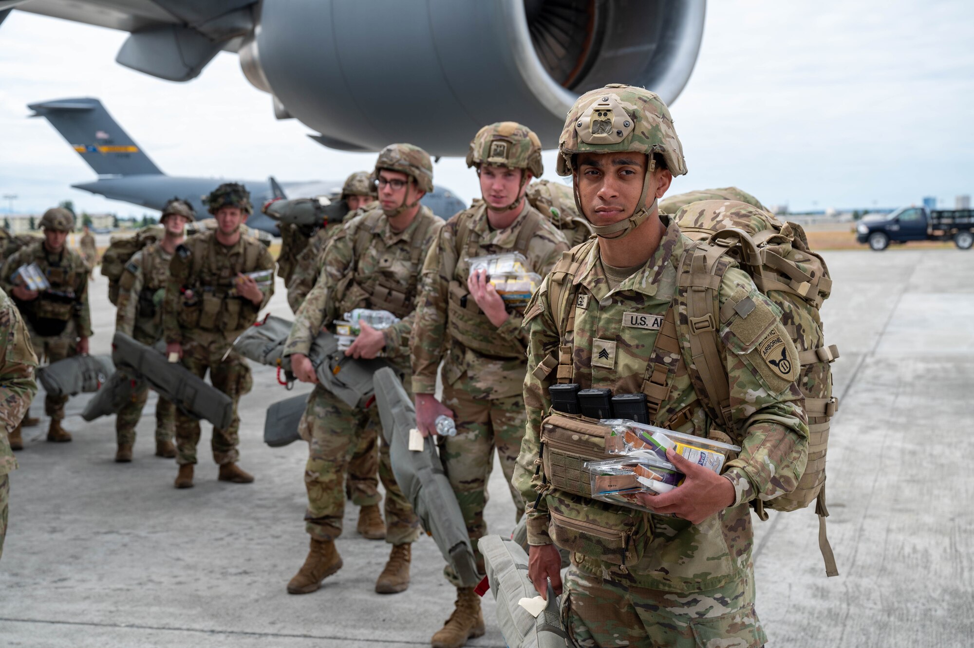 Soldiers stand outside and under a wing of a C-17.