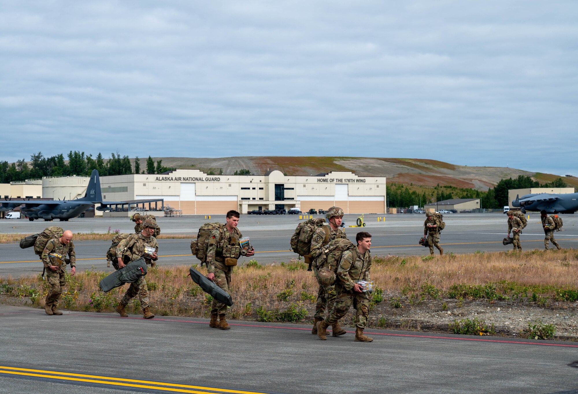 Soldiers walking on a flightline with aircraft in the background.