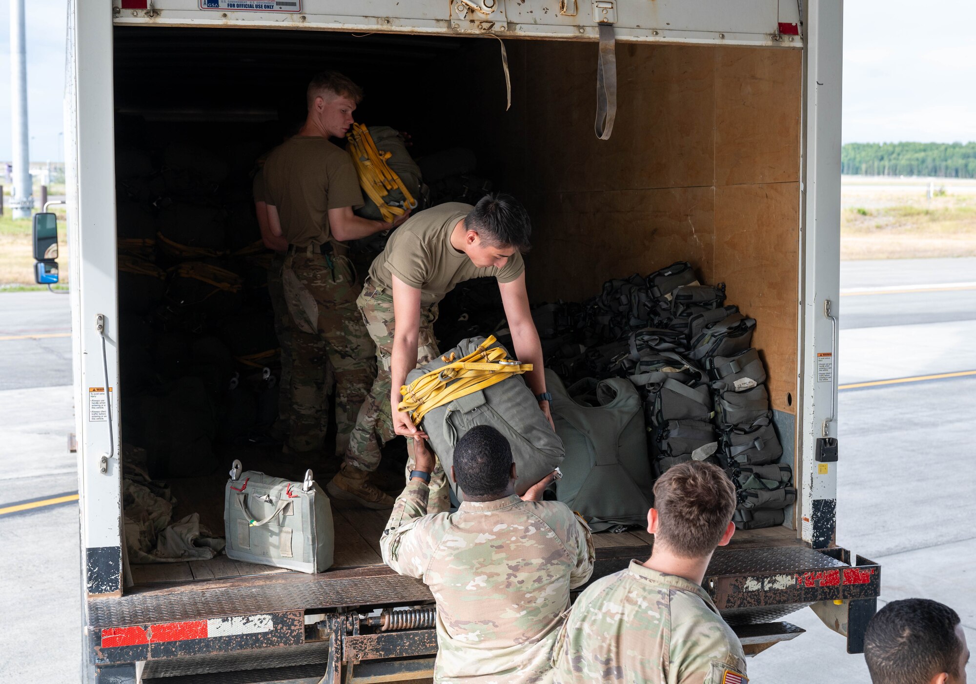 Soldiers load parachutes onto a truck on a flightline.
