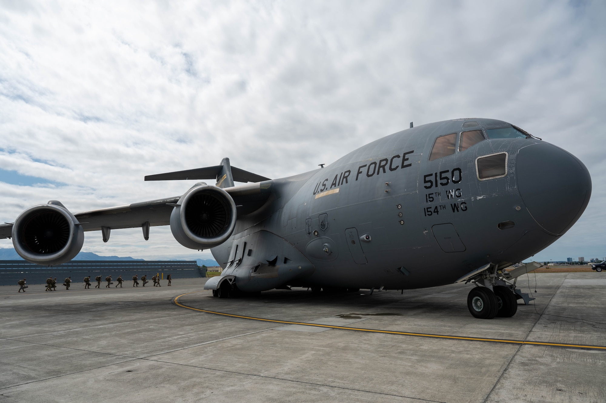 A C-17 stationed on a flightline with a small line of soldiers behind it.