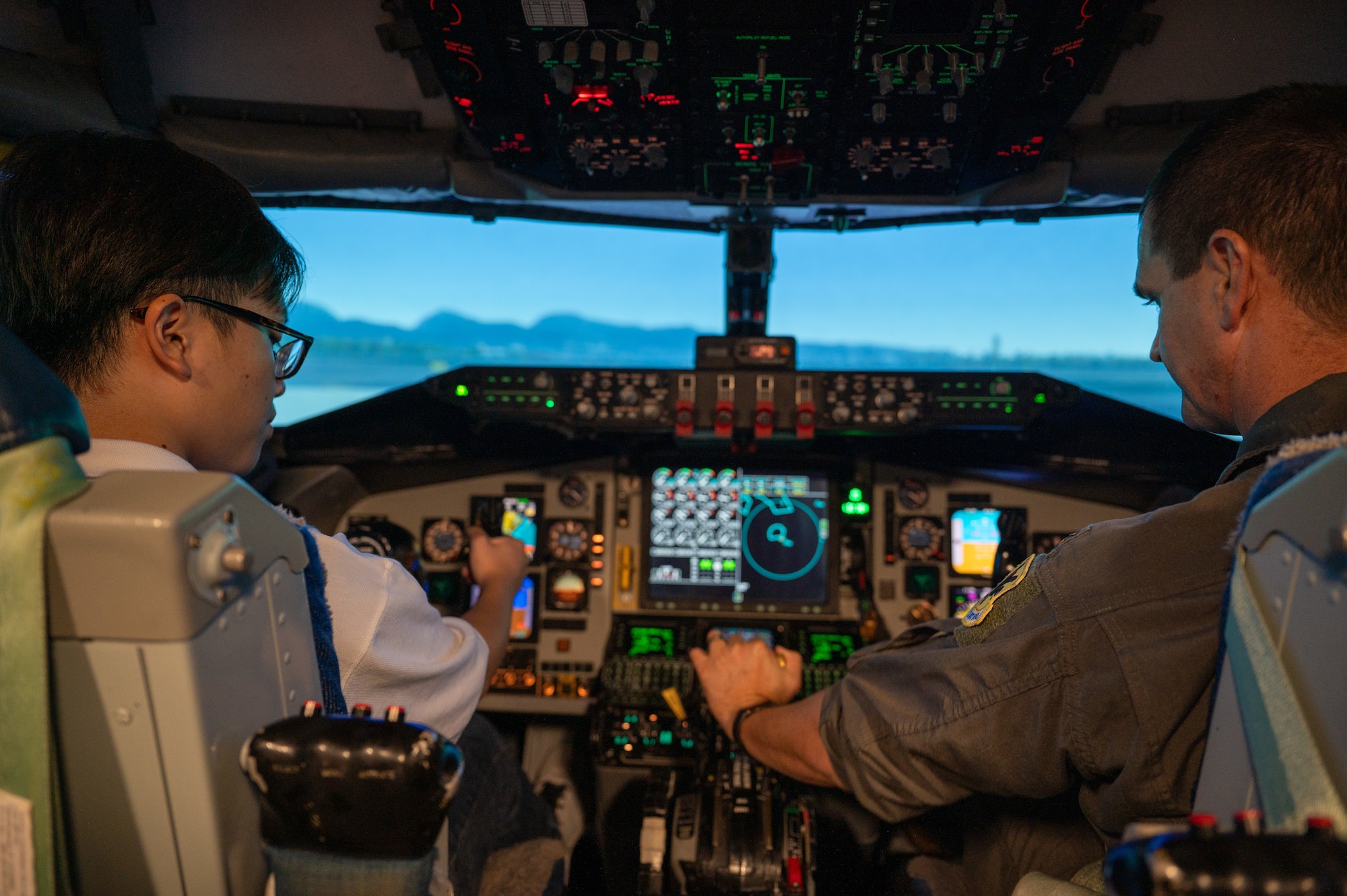 A U.S. Airmen explaining how to operate a KC-135 flight simulator to a KLI student