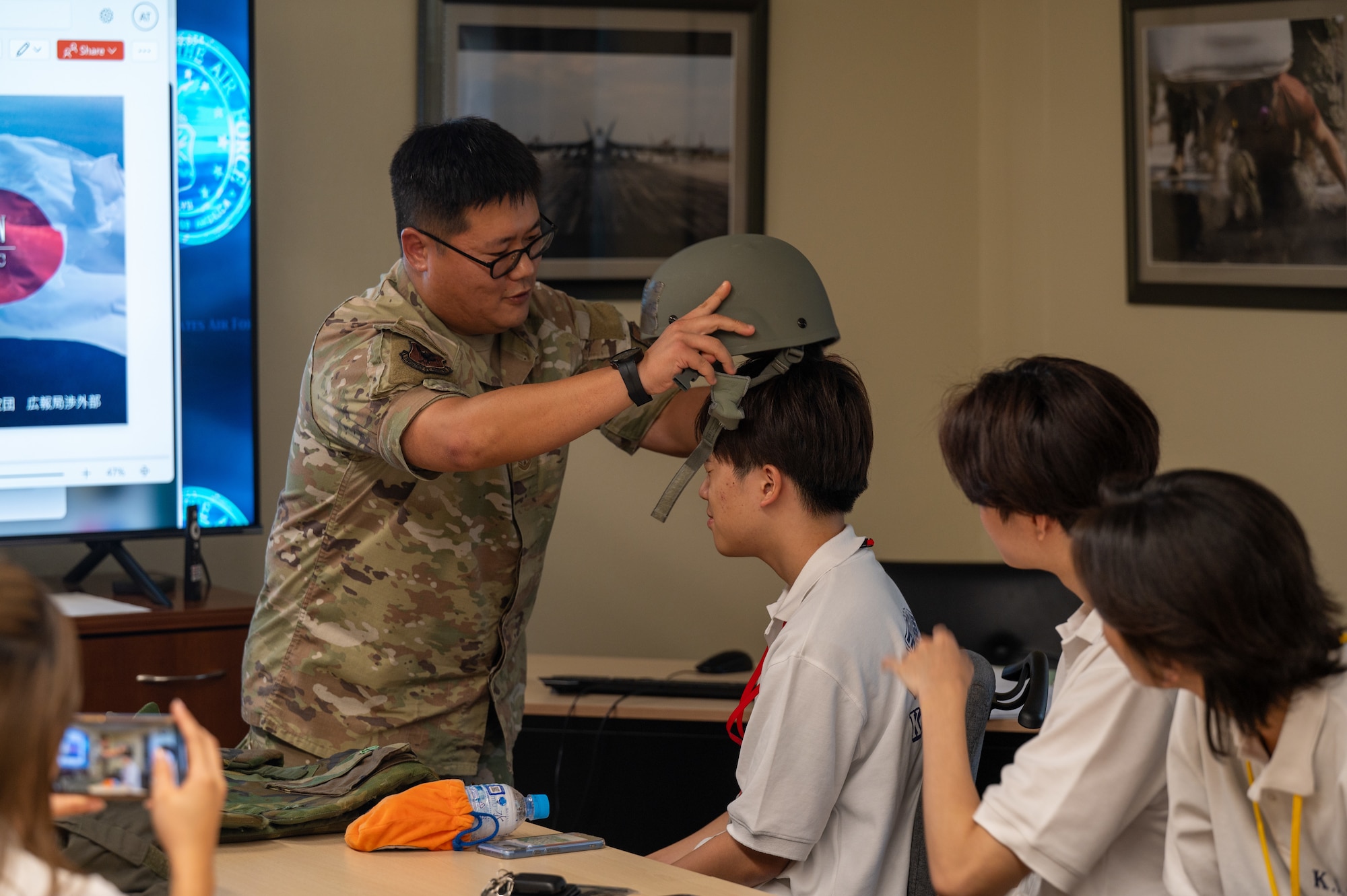 U.S. Airman places a military helmet on a KLI student's head