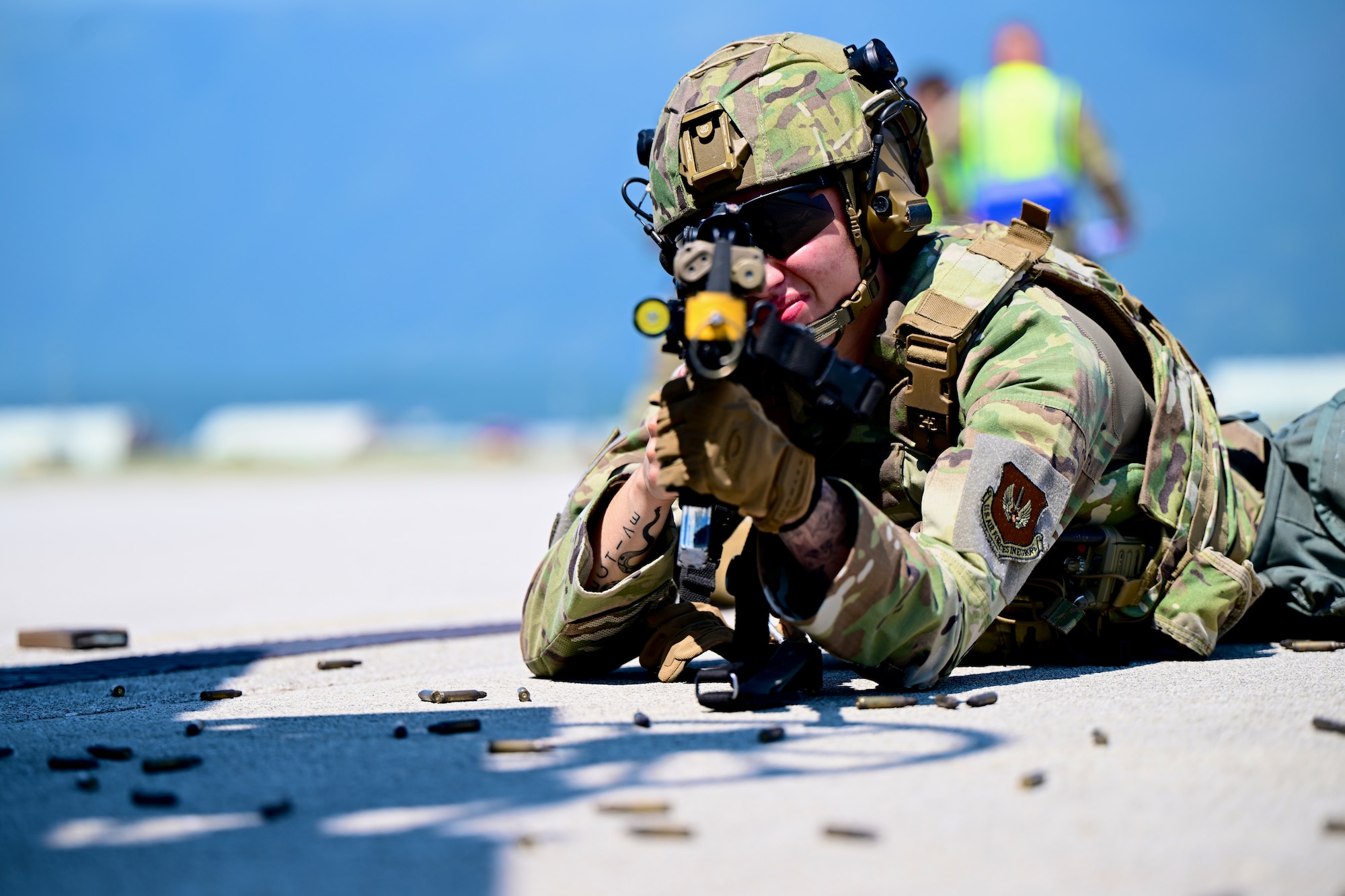 Airman lays on the ground aiming her firearm at enemy personnel.