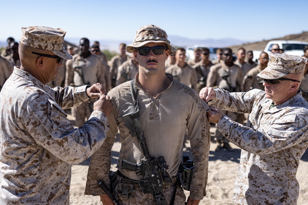 U.S. Marine Corps Sgt. Maj. Joseph Mendez, left, the sergeant major of 2d Marine Division, and Maj. Gen. Farrell J. Sullivan, the commanding general of 2d Marine Division, pins the rank of sergeant on Cpl. Adam Merrit, an infantry rifleman with 2d Battalion, 8th Marines, 2d Marine Regiment, 2d Marine Division during Service Level Training Exercise 4-25, at Marine Corps Air-Ground Combat Center, Twentynine Palms, California, July 22, 2025. SLTE 4-25 is designed to be a challenging, realistic training environment that produces combat-ready forces capable of operating as an integrated Marine Air Ground Task Force across all domains of military operations. (U.S. Marine Corps photo by Lance Cpl. Judith Ann Lazaro)