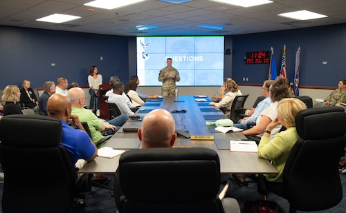 An individual military member talking to a group of individuals while giving a presentation.