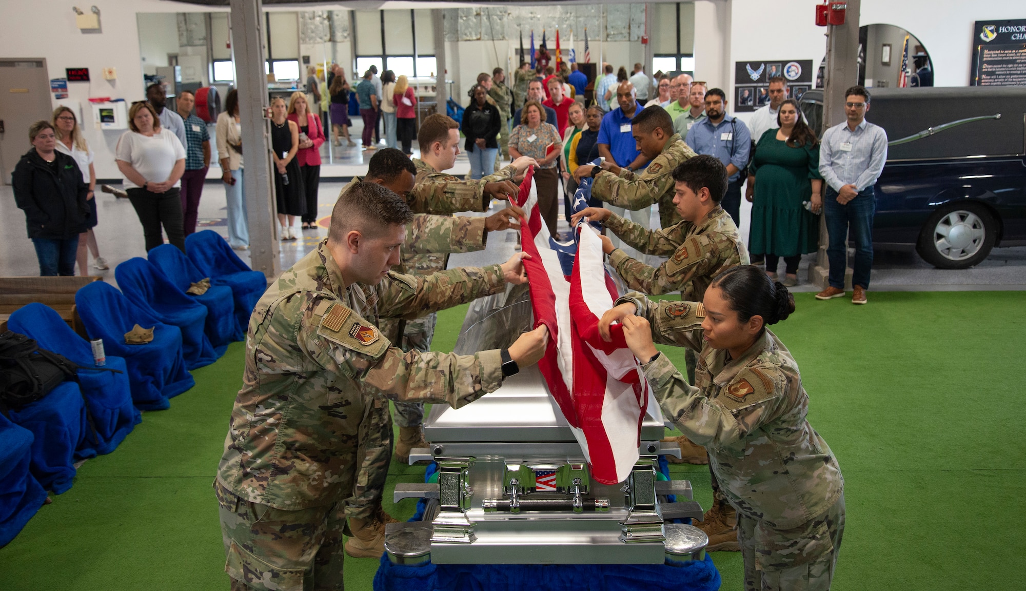Military members are holding a flag. Preparing to a fold it in front of a group of individuals.