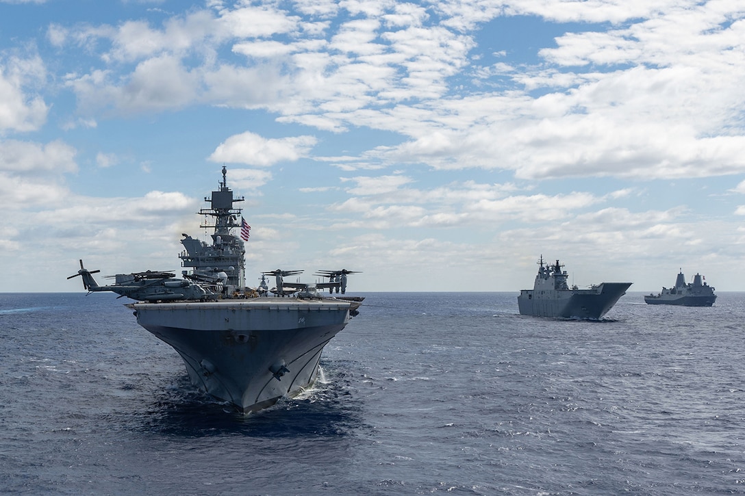 Three ships sail near each other on the ocean under partly cloud skies during the day.